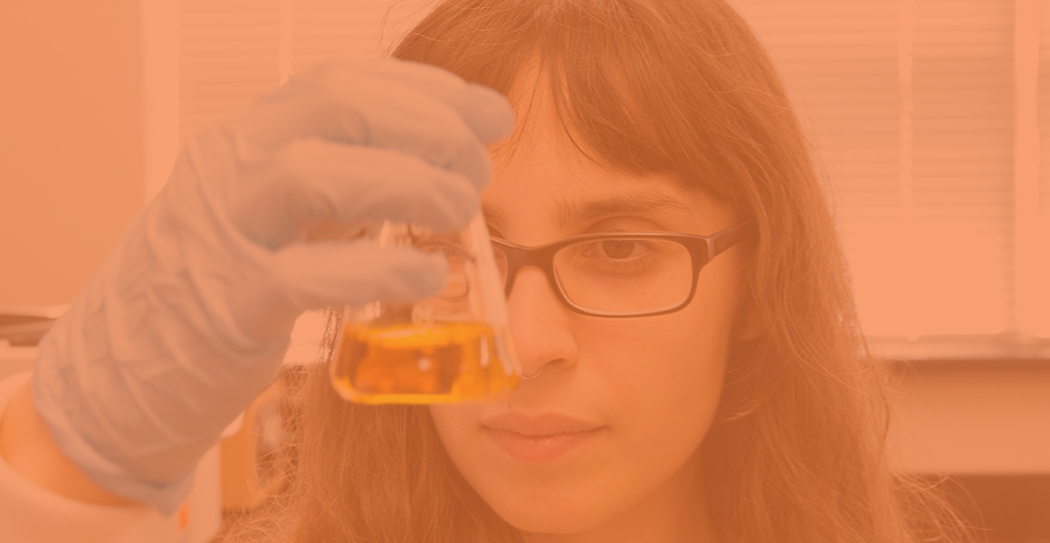 Female CALS student holding a scientific flask with yellow liquid up to eye level 
